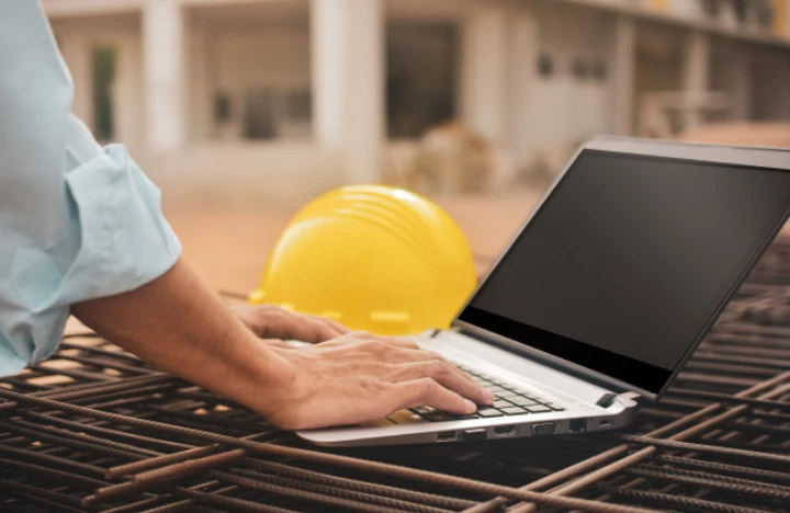 Hands on laptop in front of construction hat