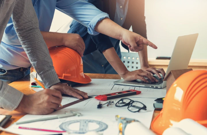 Hands pointing a blueprints in front of construction hats