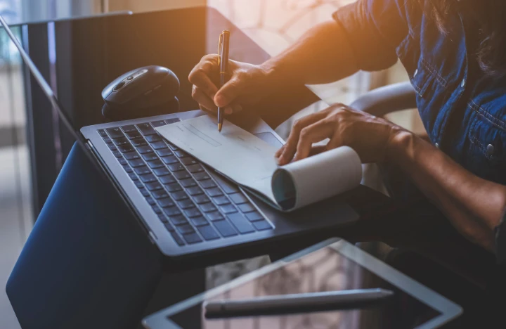 hands writing a check on top of a keyboard