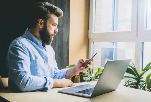 Man looking at phone in front of a laptop