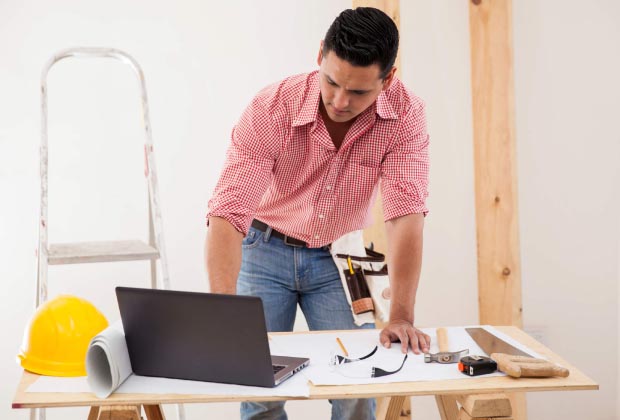 A man leaning over a laptop next to a yellow hardhat