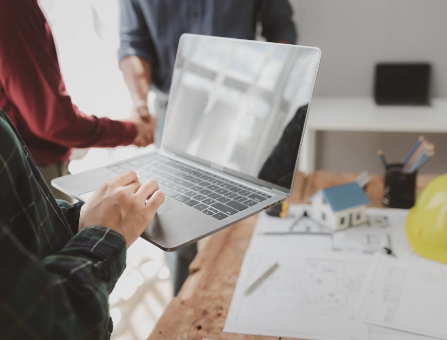 Man on a laptop while a separate pair of people in the background are shaking hands