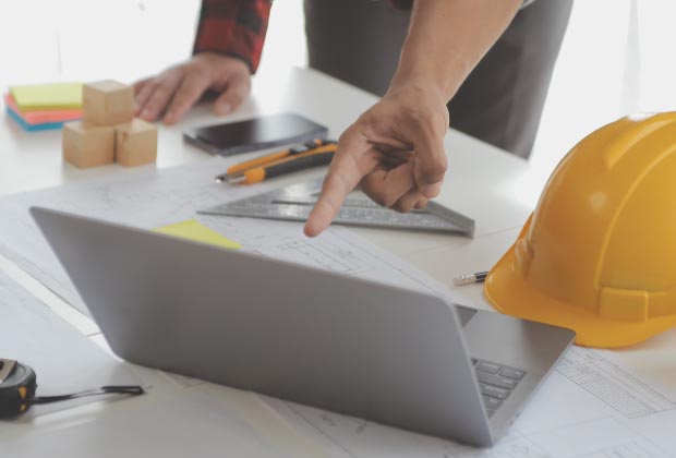 Man pointing at a laptop over some construction blueprints