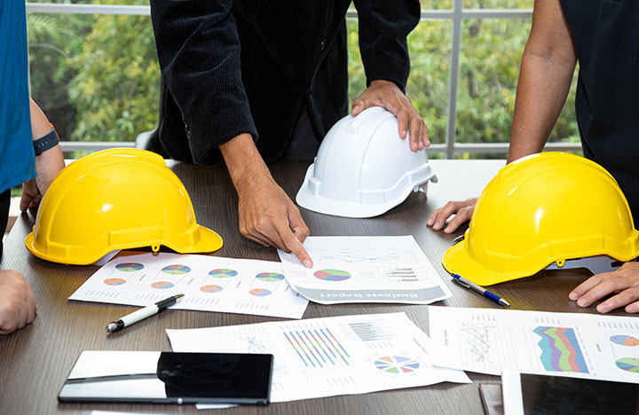 Group of people looking over pie graphs on a table with construction hats