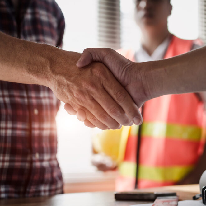 Two people shaking hands with construction worker in background